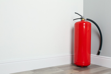 Fire extinguisher on floor in corner indoors, space for text
