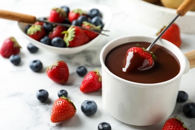 Dipping strawberry into fondue pot with chocolate on white marble table