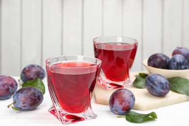 Delicious plum liquor and ripe fruits on table against white background. Homemade strong alcoholic beverage