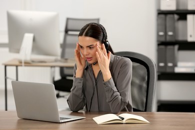Photo of Stressed hotline operator with headset working on laptop in office