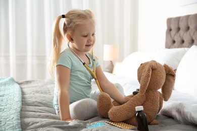 Cute child imagining herself as doctor while playing with stethoscope and toy bunny at home