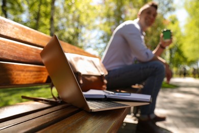 Man taking coffee break during work in park, focus on laptop