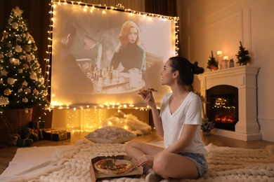 Photo of MYKOLAIV, UKRAINE - DECEMBER 24, 2020: Woman watching The Queen's Gambit series via video projector in room. Cozy winter holidays atmosphere