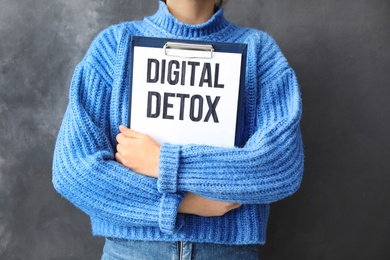 Woman holding clipboard with phrase DIGITAL DETOX on grey background, closeup