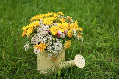 Photo of Pale yellow watering can with beautiful flowers on green grass