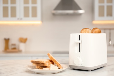 Modern toaster and bread slices on white marble table in kitchen