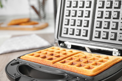 Photo of Modern iron with tasty Belgian waffles on table, closeup