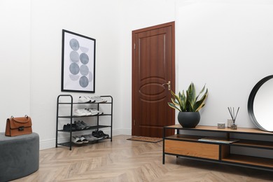 Shelving unit with shoes near white wall in hall