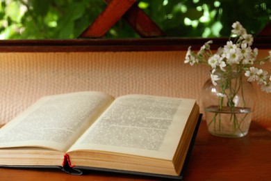 Open book and beautiful white flowers on wooden table, closeup