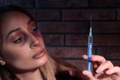 Drug addicted woman with syringe near brick wall, focus on hand