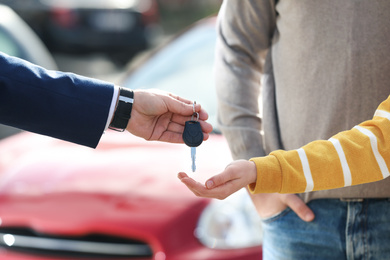 Photo of Salesman giving key to customers in modern auto dealership, closeup. Buying new car