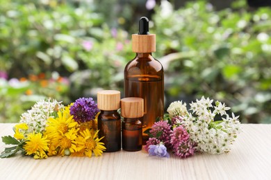 Bottles of essential oil and different flowers on white wooden table outdoors