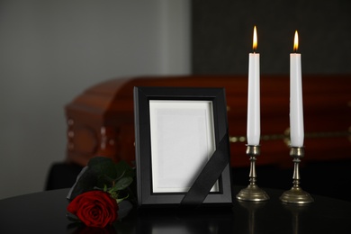 Black photo frame with burning candles and red rose on table in funeral home