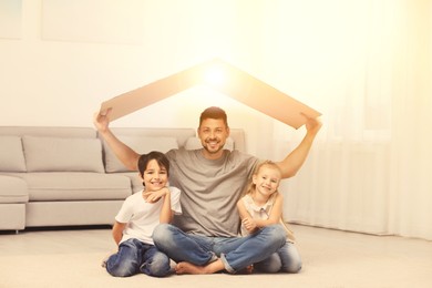 Happy father and his children sitting under cardboard roof at home. Insurance concept