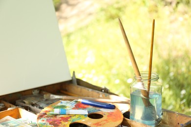 Easel with canvas and painting equipment outdoors, closeup