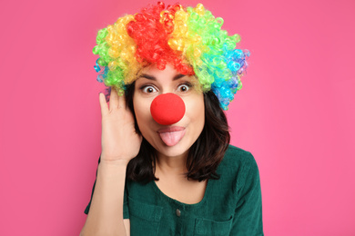 Funny woman with rainbow wig and clown nose on pink background. April fool's day