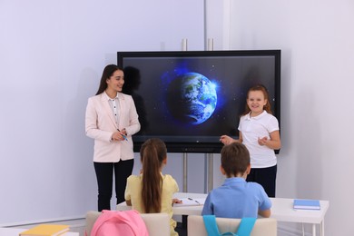 Teacher and pupil near interactive board in classroom during lesson