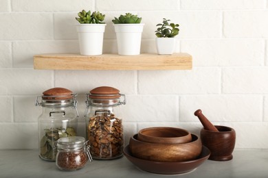 Wooden dishware and different products on grey table near white brick wall in kitchen