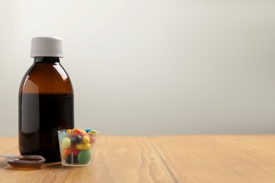 Photo of Bottle of syrup, dosing spoon and measuring cup with pills on wooden table against white background, space for text. Cold medicine