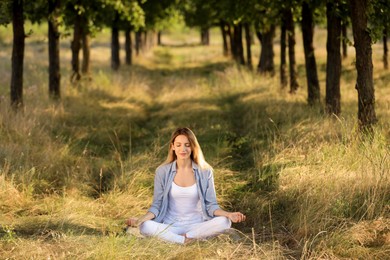 Young woman meditating in forest on sunny day
