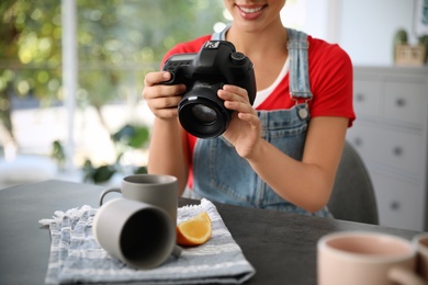 Young photographer taking picture of cups at table indoors, closeup