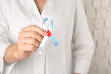 Doctor holding light blue ribbon with paper blood drop, closeup. World Diabetes Day