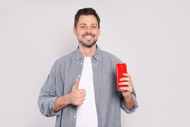 Happy man holding red tin can with beverage and showing thumb up on light grey background