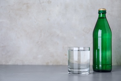 Glass and bottle with water on table against grey background, space for text