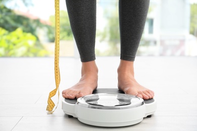 Woman with tape standing on scales indoors. Overweight problem