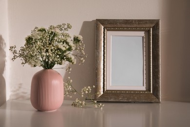 Empty photo frame and vase with flowers on table indoors