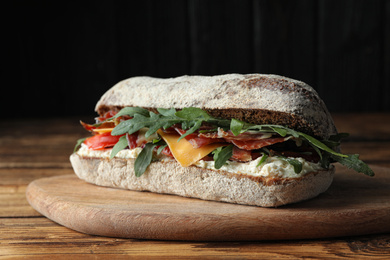 Photo of Delicious sandwich with fresh vegetables and prosciutto on wooden table