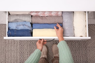 Woman opening drawer with folded clothes indoors, top view. Vertical storage