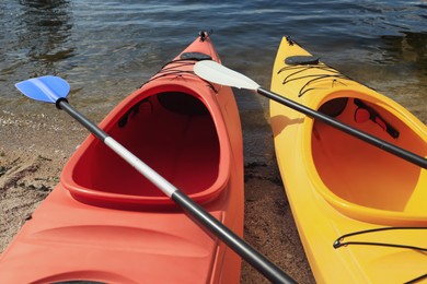 Modern kayaks with paddles on beach near river, closeup. Summer camp activity