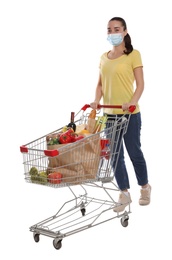 Woman with protective mask and shopping cart full of groceries on white background