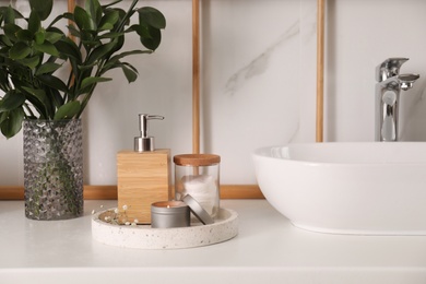 Vase with green branches, soap dispenser and cotton pads near vessel sink in bathroom