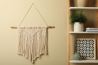 Photo of Beautiful macrame hanging on beige wall in room. Decorative element