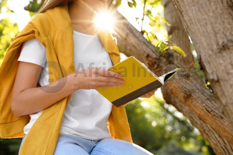 Young woman reading book near tree in park, closeup