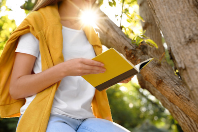 Young woman reading book near tree in park, closeup