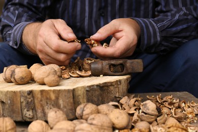 Photo of Man cracking walnuts with hammer at wooden table, closeup