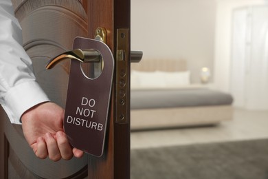 Man putting hanger on hotel door handle indoors, closeup