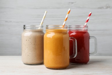 Mason jars with different tasty smoothies on white wooden table