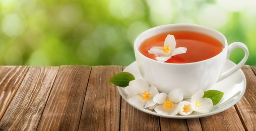Cup of jasmine tea and fresh flowers on wooden table outdoors, space for text. Banner design