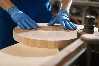 Photo of Professional carpenter grinding piece of wood in workshop, closeup