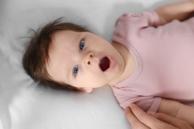 Cute baby in pink body yawning on bed, closeup