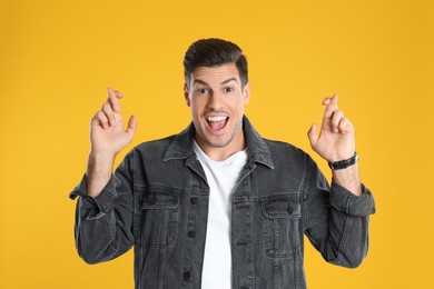 Man with crossed fingers on yellow background. Superstition concept