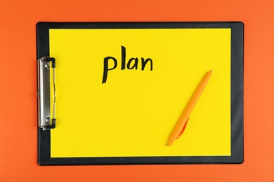 Clipboard with word Plan and pen on orange background, top view
