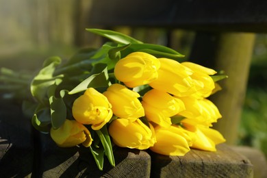 Photo of Bouquet of beautiful yellow tulips on wooden bench outdoors, closeup