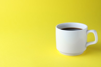 White mug of freshly brewed hot coffee on yellow background, space for text