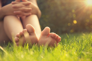 Teenage girl sitting barefoot on green grass outdoors, closeup. Space for text