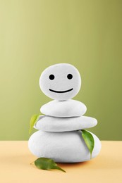 Photo of Stack of stones with drawn happy face and leaves on beige table against light green background. Zen concept